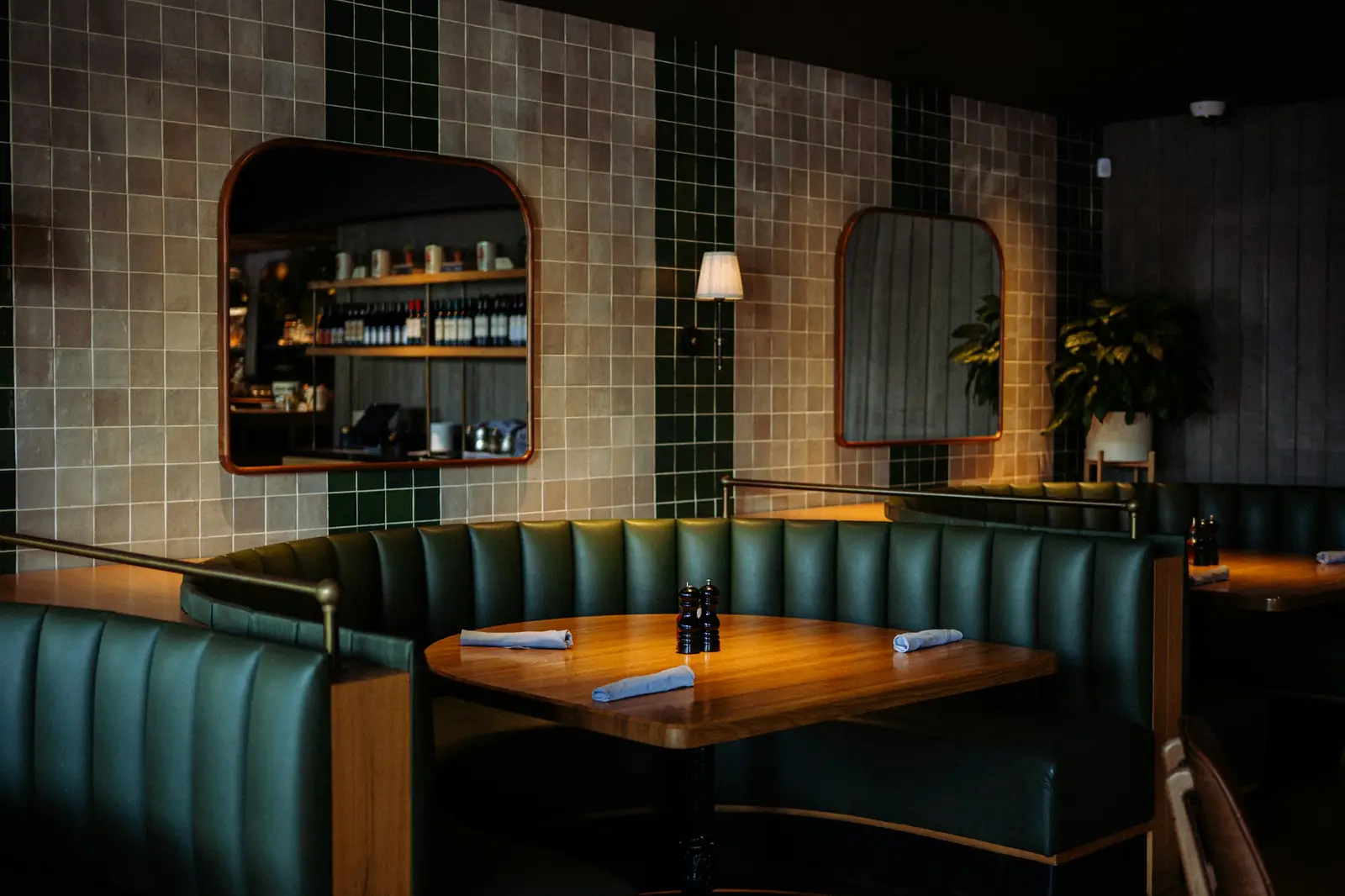 Restaurant corner with green leather banquettes and a tiled wall